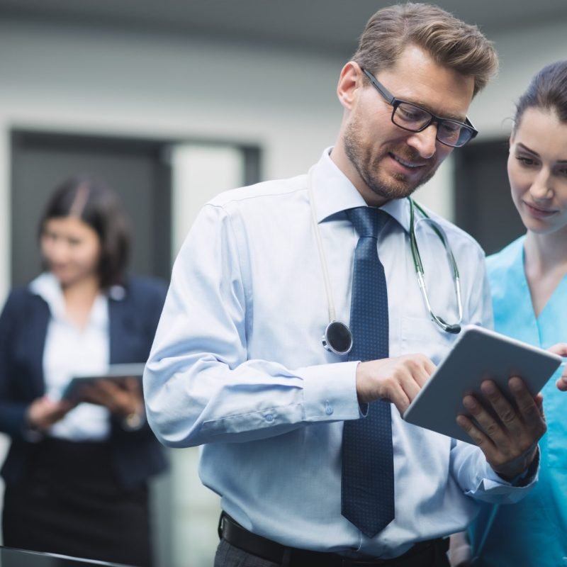 Doctor and nurse discussing over digital tablet in hospital corridor