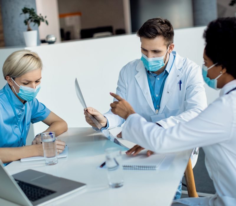 Team of medical experts examining X-ray of a patient while working at the hospital. They are wearing face masks due to COVID-19 pandemic.