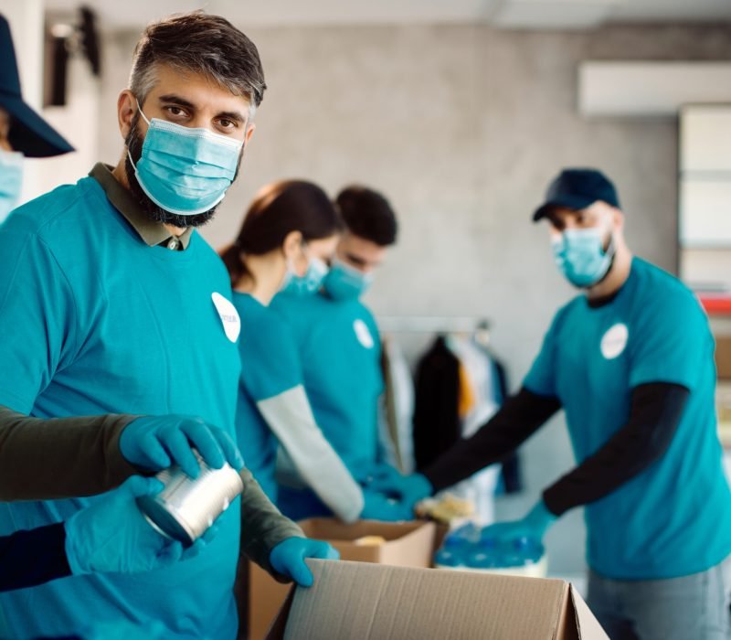 Group of volunteers packing boxes with canned food for charitable donation. Focus is on man looking at camera.
