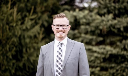 A handsome man in suit standing outdoors with blurry greenery in the background