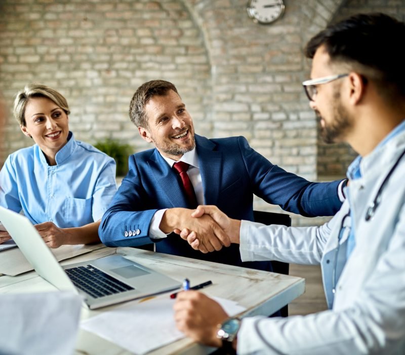 Happy financial advisor and male doctor shaking hands after successful meeting in the office.